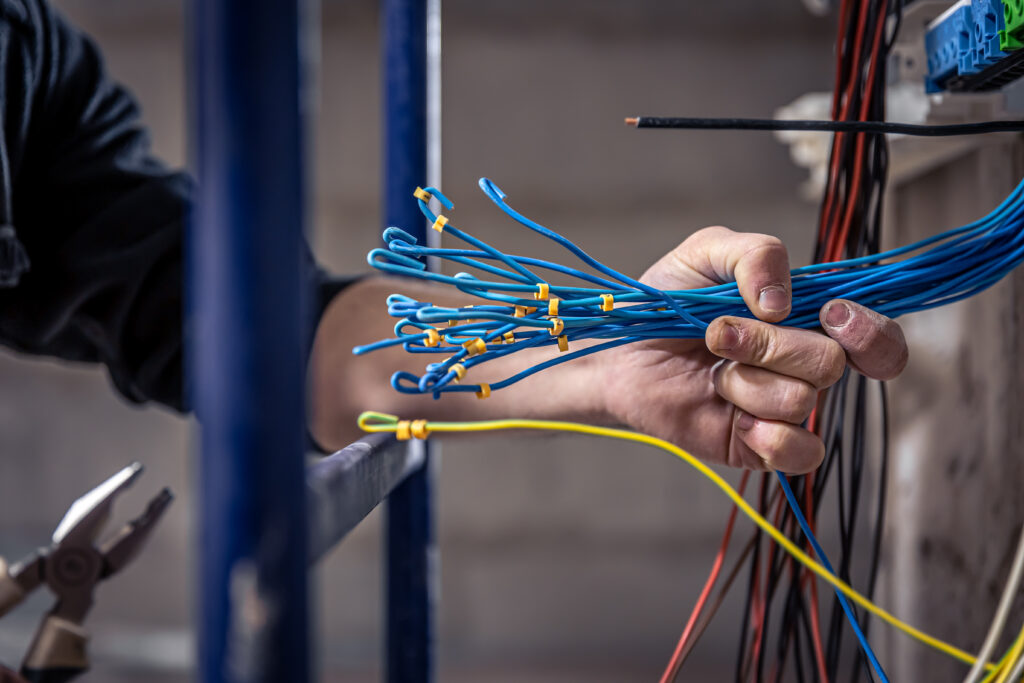 male electrician works switchboard with electrical connecting cable scaled