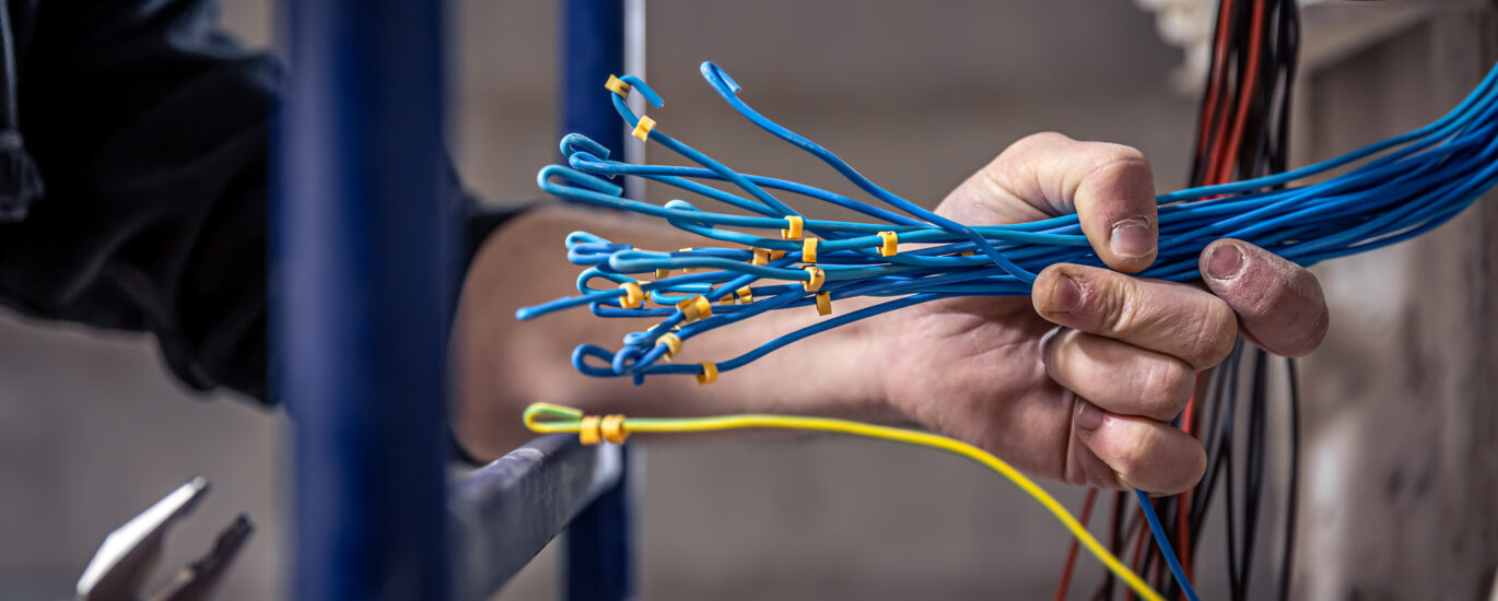 male electrician works switchboard with electrical connecting cable scaled