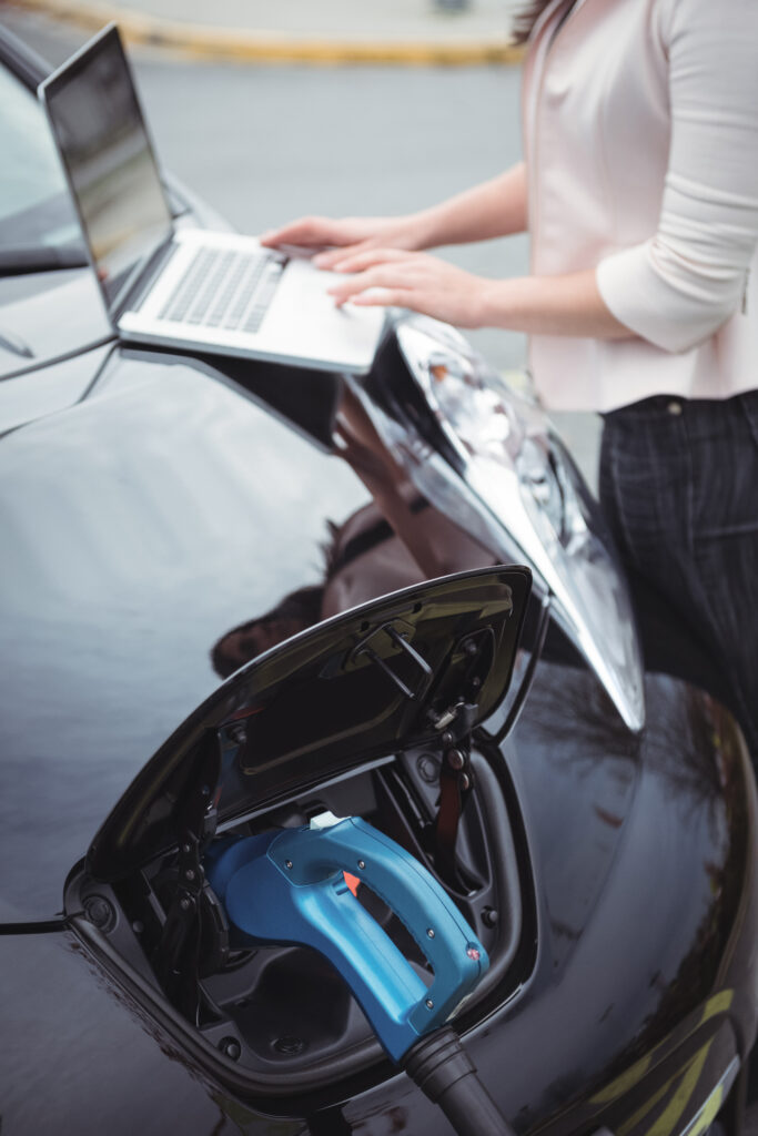 mid section woman using laptop while charging electric car scaled